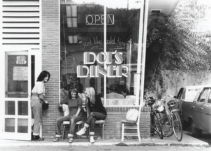 A black and white photograph of the Dot's Diner storefront, three people sitting outside the window, the lettering reading Just like old times.