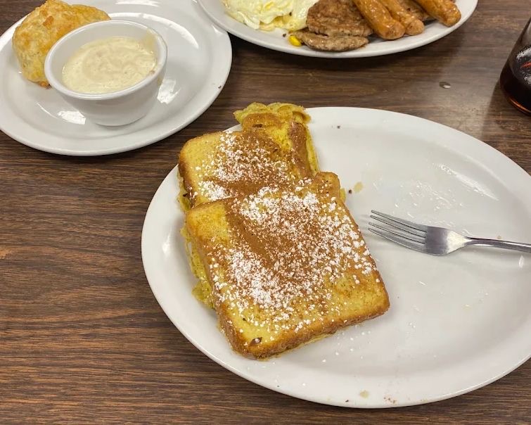 French toast at Dot's Diner, thick slices dusted with powdered sugar, with a biscuit and a cup of gravy on a second plate behind it.