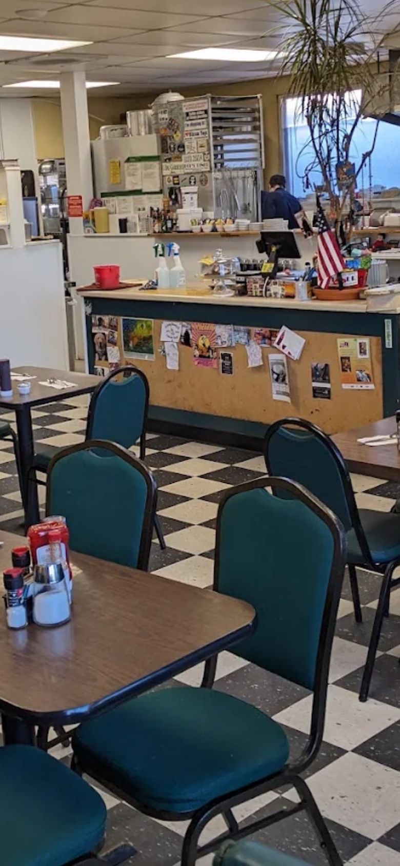 The dining room at Dot's Diner, green chairs at laminate tables on a black and white checkerboard floor.